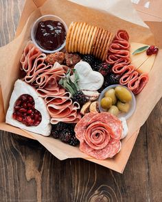 an assortment of meats and cheeses in a cardboard box on a wooden table