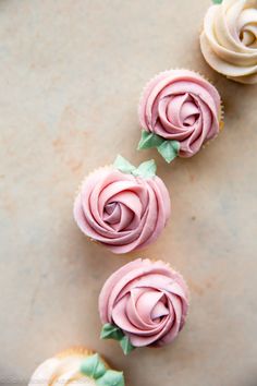 three cupcakes with pink frosting and green leaves