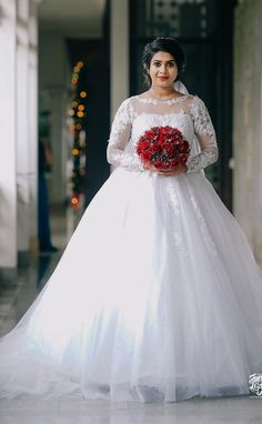 a woman in a white wedding dress holding a red bouquet and posing for the camera