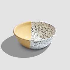 a white and yellow bowl with black speckles on the side, sitting in front of a gray background