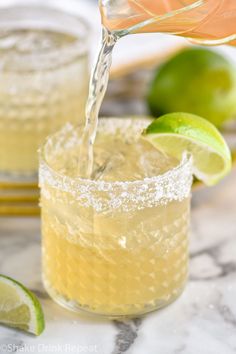 a margarita being poured into a glass with limes and sugar on the rim next to it