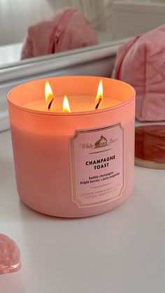 a pink candle sitting on top of a white counter next to a mirror and soap