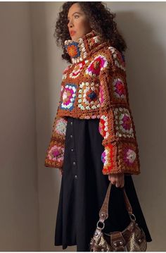 a woman in a crocheted jacket holding a purse and looking off into the distance