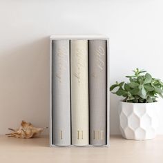 two books sitting on top of a wooden table next to a potted plant and a white vase