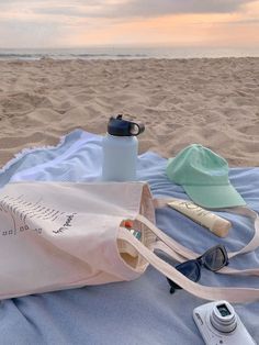 a beach towel, water bottle and sunglasses on the sand