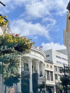 a woman standing in front of a building with flowers hanging from it's balconies