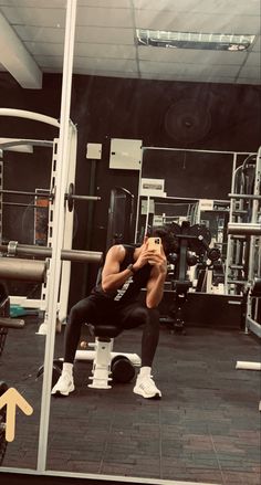 a man squats in the middle of a gym while taking a photo with his cell phone