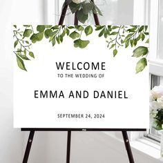 a welcome sign with flowers and greenery on it in front of a white window