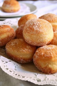 some sugared donuts are on a white lace doily next to another plate