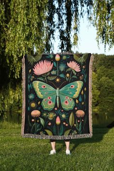 a woman standing in front of a tree holding a blanket with a butterfly on it