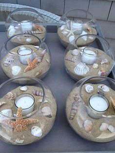 there are four glass dishes with seashells and candles in them on the table