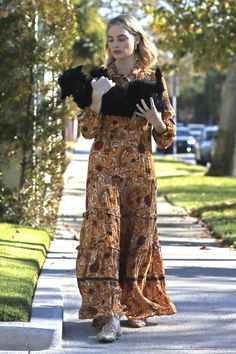 a woman is walking down the street with her dog in her arms and she's wearing a floral jumpsuit