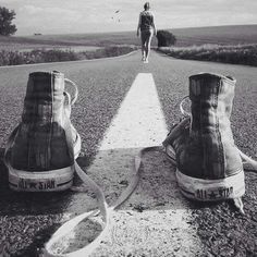 a person walking down the middle of an empty road with two pairs of shoes on it