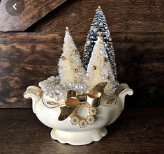 two small white christmas trees in a teapot with pearls and bows on the top