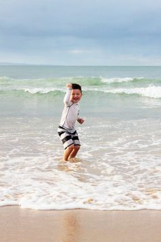 a young boy is running in the water at the beach