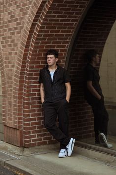 a young man leaning against a brick wall