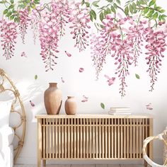 a wall with pink flowers on it next to a wooden cabinet and wicker chair