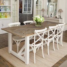 a dining room table with white chairs and a vase on top of it in front of a large mirror