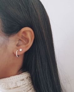 a woman wearing a star and moon earring on her left ear, looking down at the ground