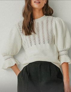 a woman is wearing a white sweater and black pants with her hands on her hips