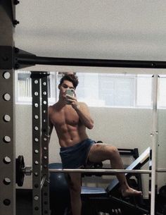 a shirtless man taking a selfie with his cell phone in a gym setting