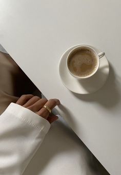 a cup of coffee sitting on top of a white table next to a person's hand