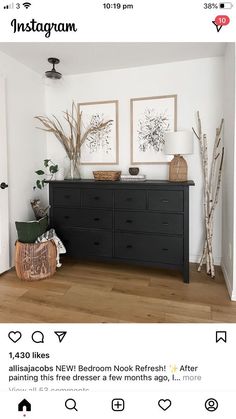 a black dresser with two pictures on the wall above it and some branches in front of it