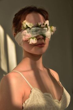 a woman with flowers on her face and veil over her eyes, wearing a white dress