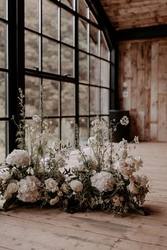 white flowers and greenery are arranged on the floor in front of a large window