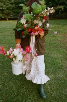 a woman holding flowers in a bucket on the grass