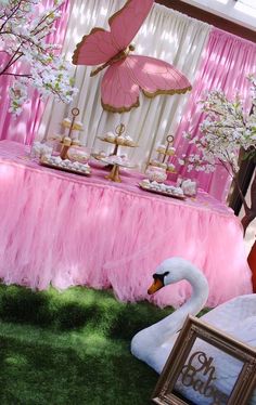 a table with pink and gold decorations on it, including a swan cake stand in the middle