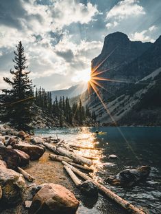 the sun shines brightly through the clouds over a mountain lake with rocks and logs