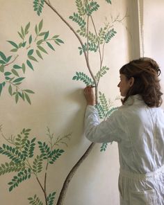 a woman painting a tree on the wall with green leaves and branches painted on it