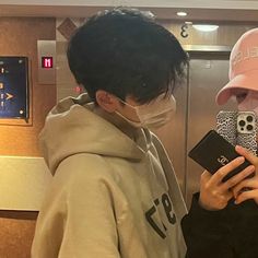 two people wearing face masks and looking at their cell phones while standing in an elevator