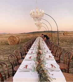 a long table is set with plates and place settings for an outdoor dinner in the middle of a field