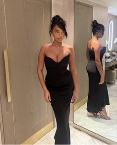 a woman standing in front of a mirror wearing a black dress