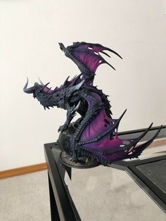 a purple dragon statue sitting on top of a black table next to a white wall