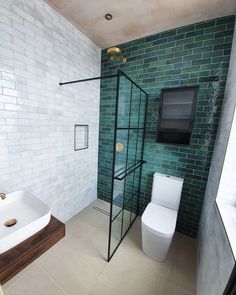 a bathroom with a toilet, sink and shower in it's stall area next to a green tiled wall