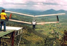 a man standing on top of a wooden platform next to an airplane flying in the sky