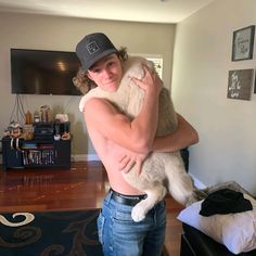 a man holding a cat in his arms and smiling at the camera while wearing a hat