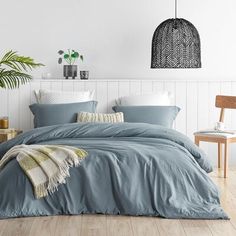 a bed with blue sheets and pillows in a white room next to a wooden chair