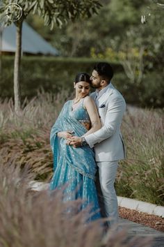 a man and woman standing next to each other in front of some tall grass covered bushes