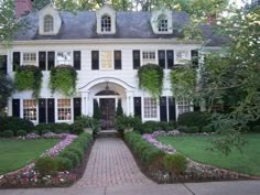 a large white house with black shutters and lots of flowers in the front yard