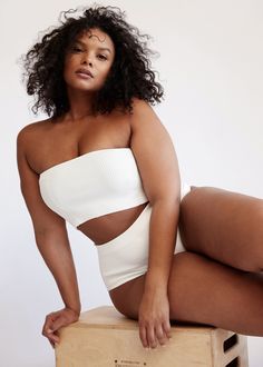 a woman sitting on top of a wooden box wearing a white bodysuit and high heels