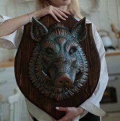 a woman holding up a wooden plaque with a pig on it's face in the shape of a boar