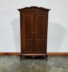 a wooden armoire sitting on top of a floor next to a wallpapered wall