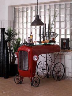 a red cart sitting in front of a window next to a lamp and potted plant