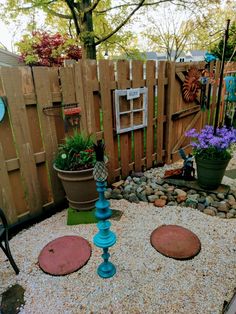 an outdoor garden with gravel, rocks and potted plants on the ground in front of a wooden fence