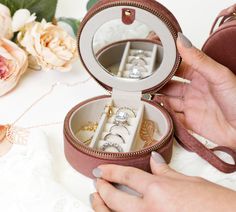 a woman holding an open ring box with jewelry inside it on a table next to flowers