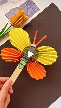 a hand holding a paper butterfly on top of a table